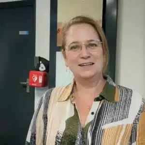 Woman with glasses pointing to a red wall-mounted AED.