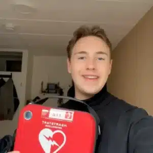 Young man holding red AED and smiling at the camera indoors.