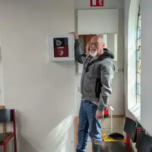 Man pointing at a red AED mounted beside a window.