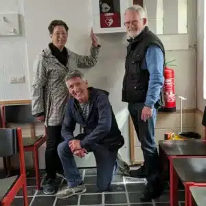 Three adults pointing to an AED mounted on an indoor wall.