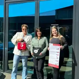Three people standing outdoors with AED and information poster.